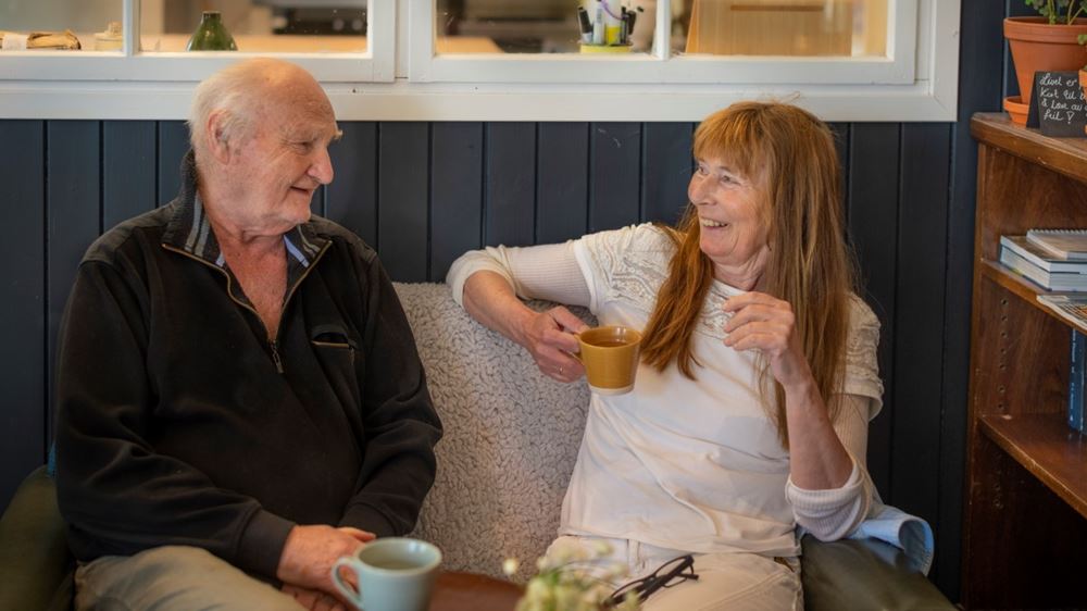 En eldre mann og dame sitter i en sofa, ser på hverandre og snakker sammen.