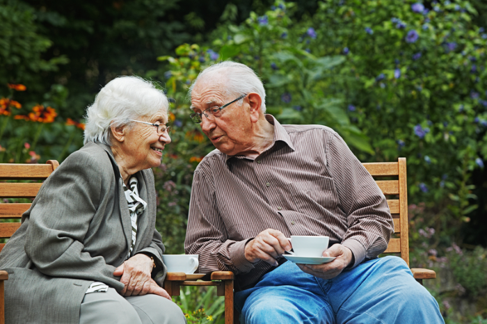 To eldre mennesker på en benk som drikker kaffe