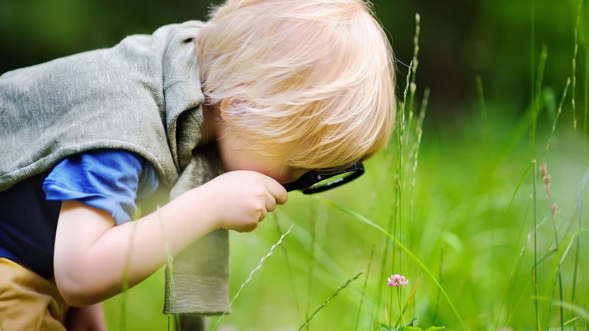 Gutt med forstørrelsesglass gransker gresset.