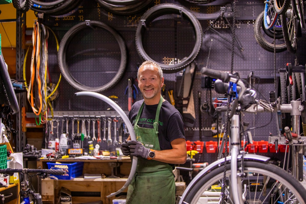 Mann som viser frem sykkeldekk i en sykkelbutikk der alt er brukt.. 
