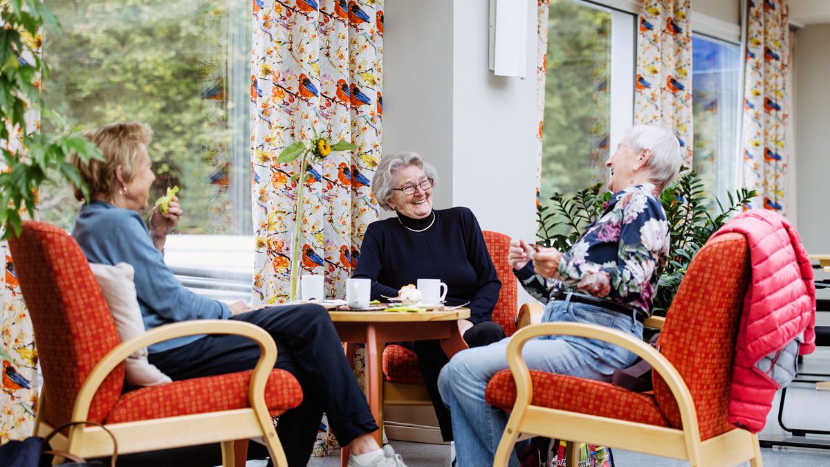 Tre smilende kvinner rundt bord på Holmen innbyggertorg