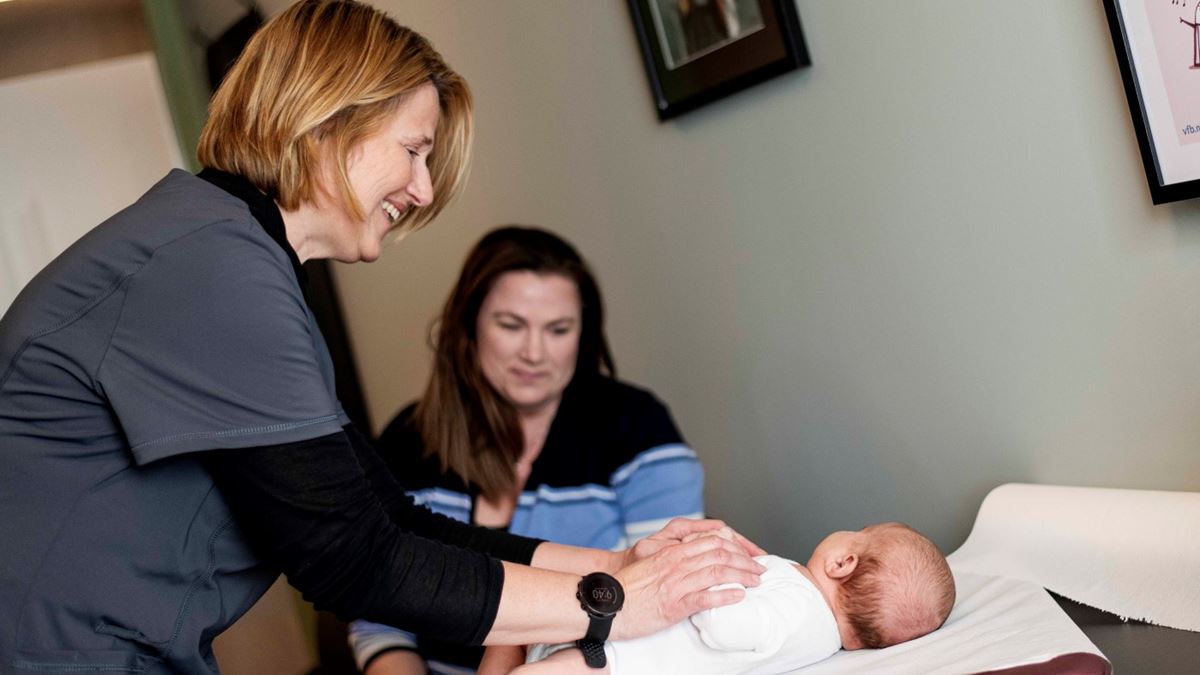 Helsesøster hjelper mor og barn på helsestasjon