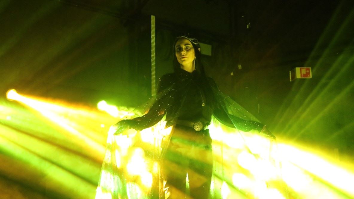 scenebilde, med en sterk og gul lysstråle som treffer en person kledd i svart. Mørk bakgrunn.