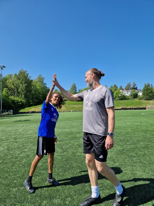 En dame i en blå fotballdrakt tar high five med en høy mann i trenerdrakt.