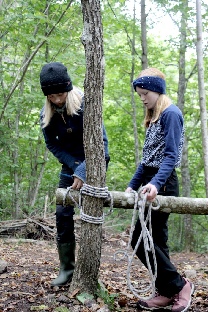To jenter holder en trestokk som de fester med tau til et tre.