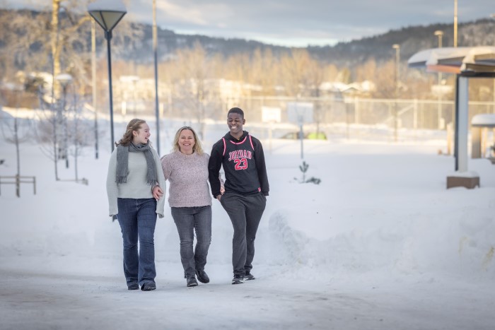 En dame går arm i arm med to ungdommer, en gutt og en jente, ute i snøen. De ser på hverandre og smiler. 
