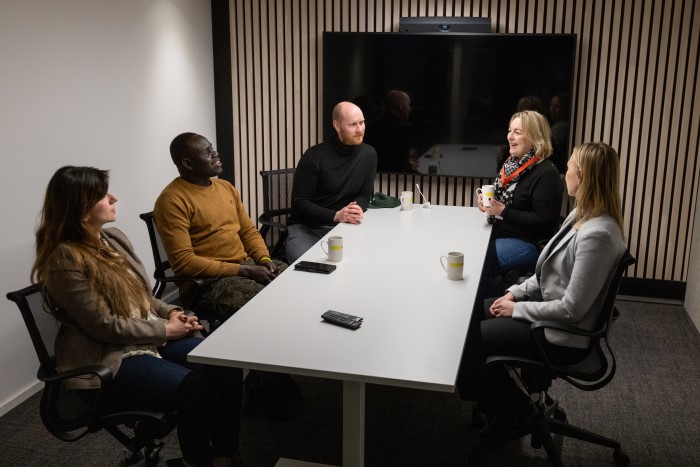 Fem personer sitter sammen rundt et møtebord. Alle ser mot personen lengst inn i rommet. I bakgrunnen er et stor svart skjerm.