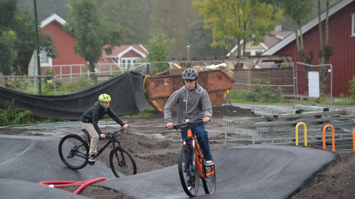 To gutter med hjelm på hodet sykler på hver sin sykkel i en pumptrack-bane. Begge ser konsentrert ut.