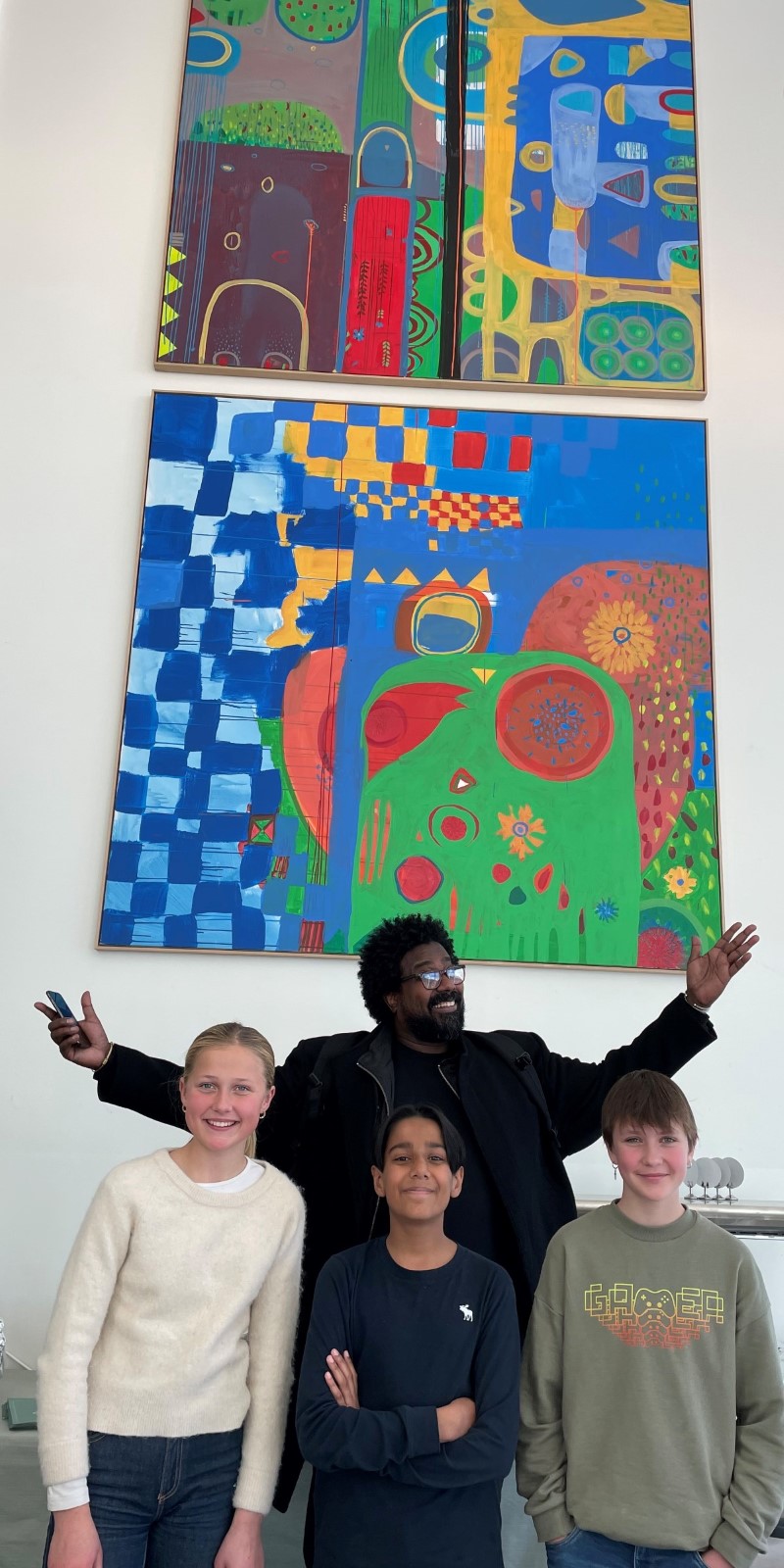 Tre barn og en mann står samlet foran en vegg med fargerike malerier over seg. Alle fire ser mot kamera og smiler.